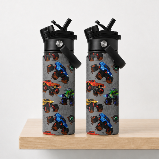 reusable water bottles with black lids and straws, standing side by side on a light wood surface against a plain light gray background. The bottles have a gray printed body covered in colorful monster truck illustrations.