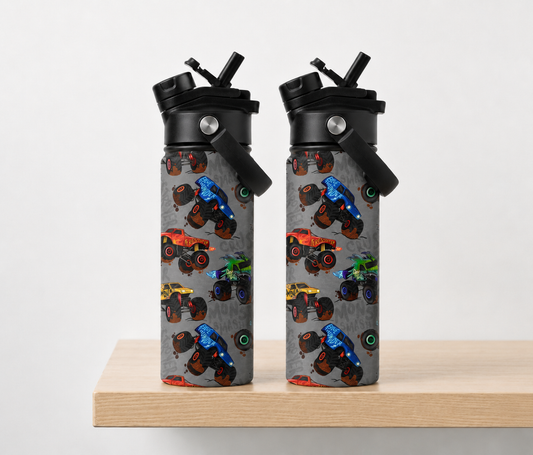 reusable water bottles with black lids and straws, standing side by side on a light wood surface against a plain light gray background. The bottles have a gray printed body covered in colorful monster truck illustrations.